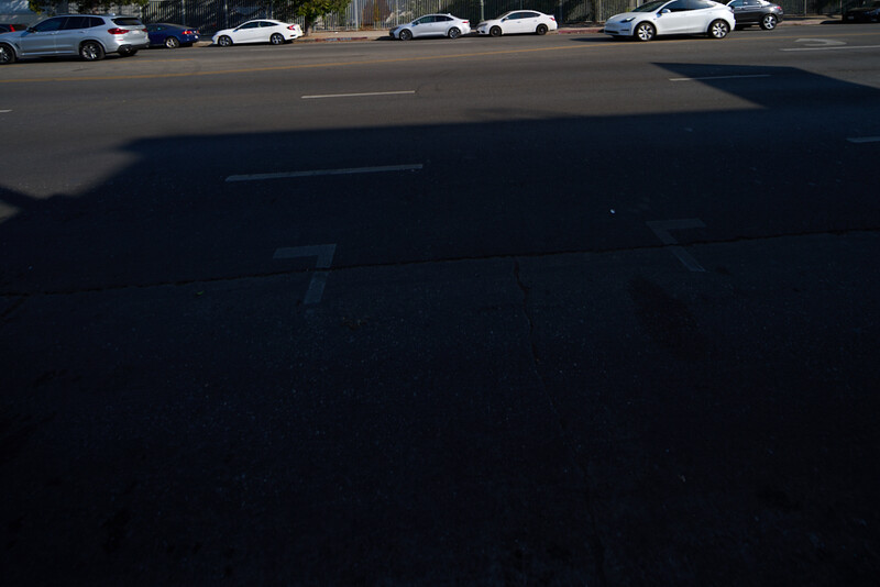 Parking lot with vehicles under bright sunlight casting strong shadows across asphalt.