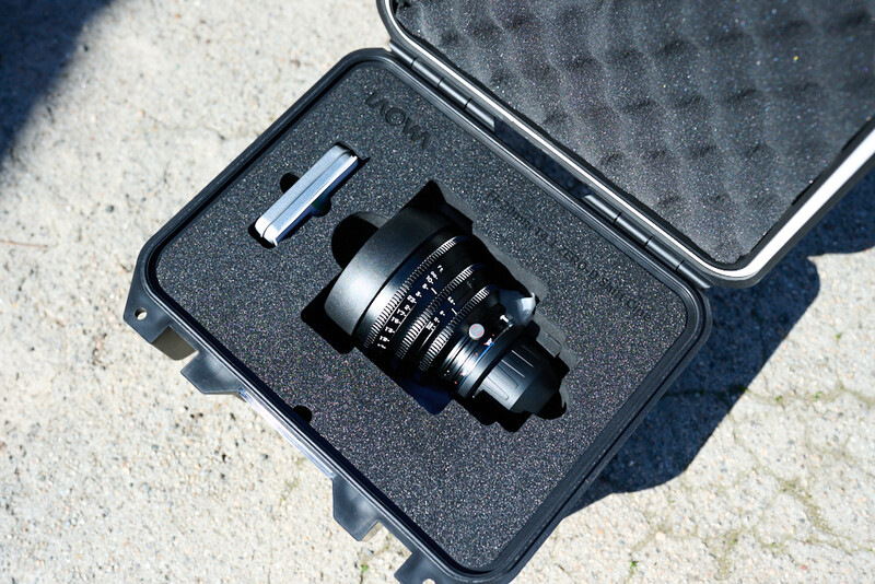 Black manual focus lens with hood nestled in custom foam case insert on concrete surface.