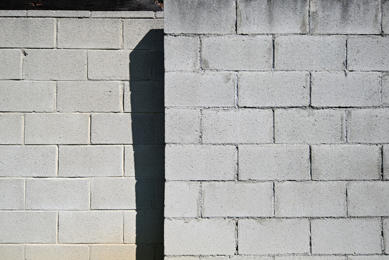 Two concrete block walls meeting at a vertical edge, with strong directional shadow creating stark contrast between light and dark surfaces.