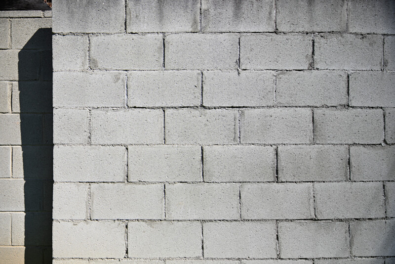 Concrete cinder block wall with strong shadow from vertical edge, showing texture and mortar joints.