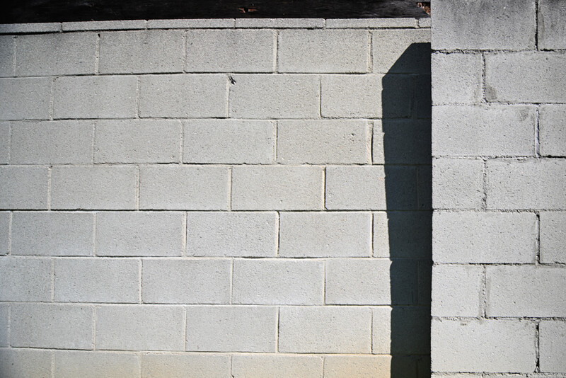 Dark vertical pipe or conduit against light-colored concrete block wall with strong shadow.