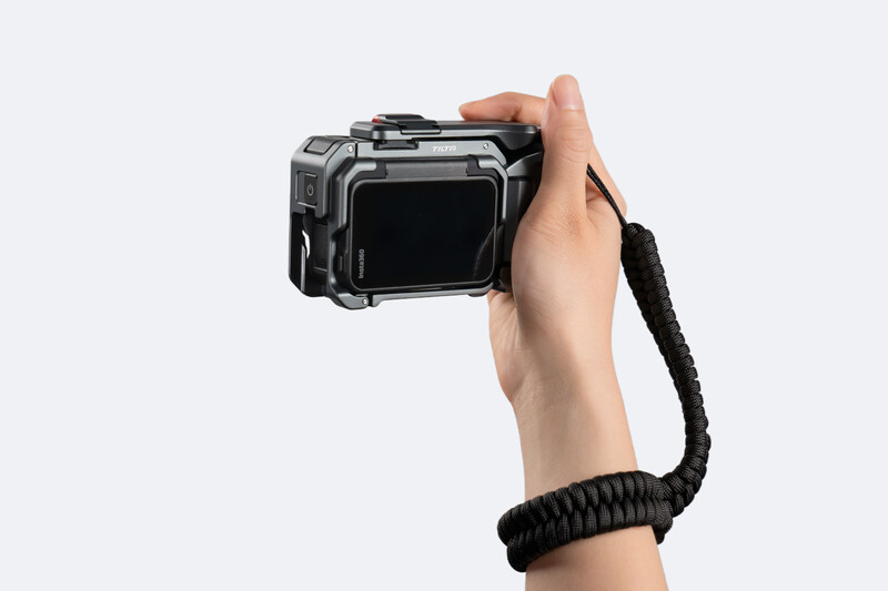 Hand holding a compact action camera with black wrist strap against white background.