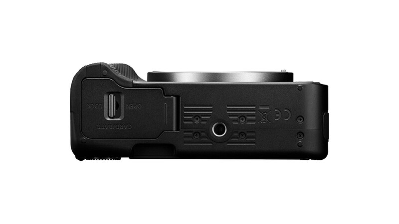 Bottom view of a black mirrorless camera body showing battery compartment, ports, and tripod socket.