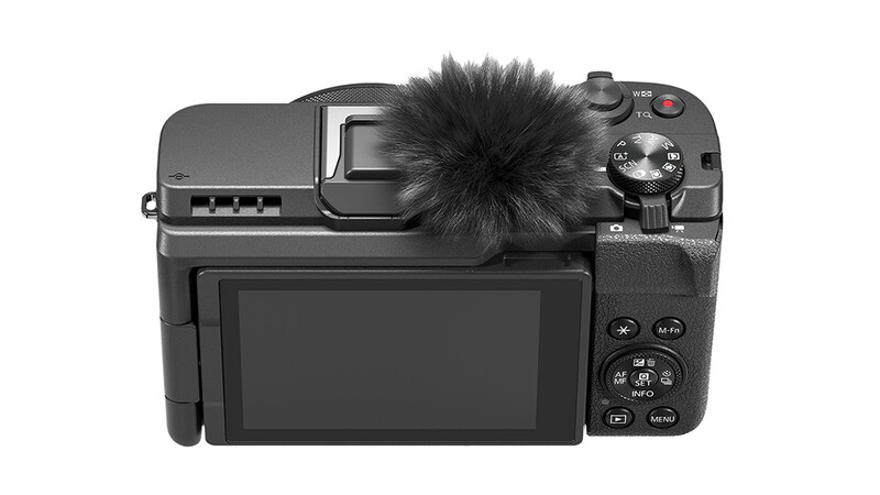 Rear view of a compact mirrorless camera with articulating LCD screen and windscreen microphone attachment.