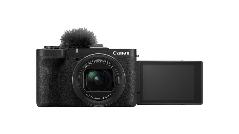 Canon PowerShot compact camera with articulating screen and shotgun microphone attachment.
