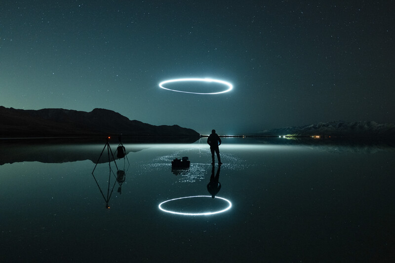 Silhouetted figure standing on frozen water with two glowing neon circles hovering above and reflected below.