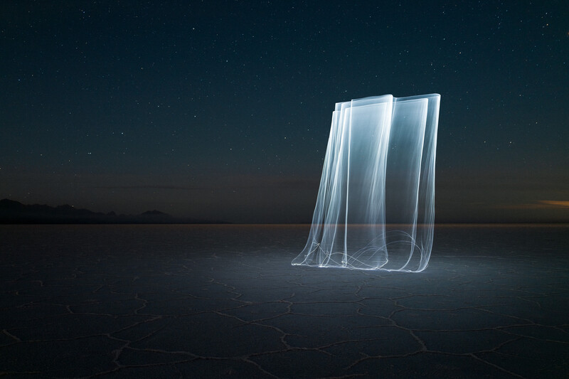 Luminous translucent fabric structure standing alone on a dark frozen landscape under a starlit sky.