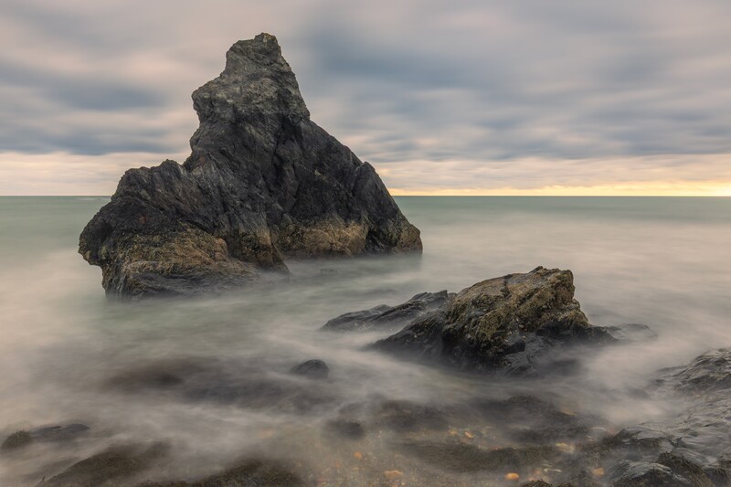 Dramatic rocky sea stacks rise from misty water under a cloudy sky at dusk.