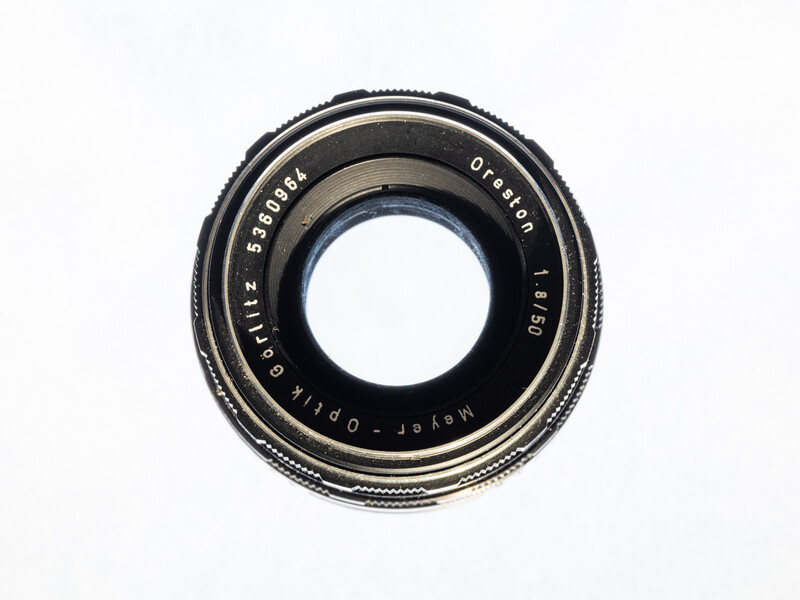 Vintage camera lens with glass elements visible through center opening against white background.