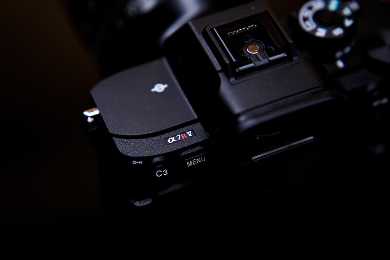 Sony Alpha camera body with menu button visible, displayed among photography equipment in low-key lighting.