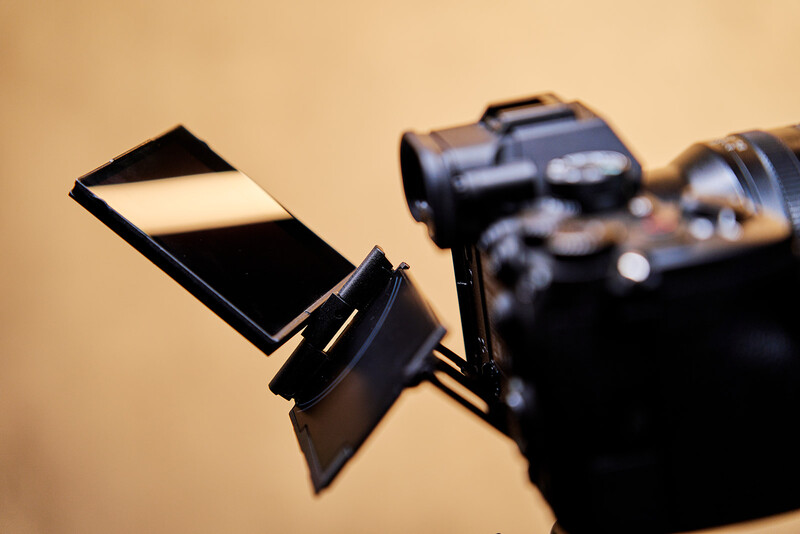 Camera flash diffuser attachment mounted on a camera body against a warm, neutral background.