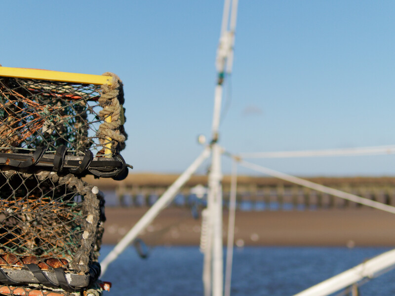 Weathered lobster trap in sharp focus with wind turbine and waterway blurred in background.