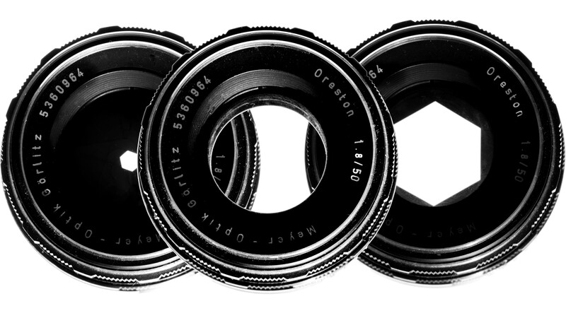 Three vintage camera lenses arranged in a row, displaying glass elements and aperture blades in their optical centers.