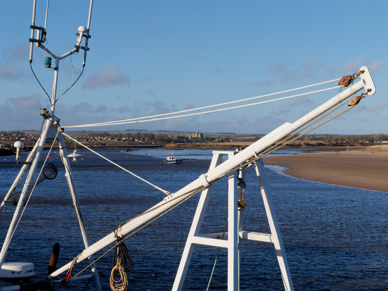 Telescopic camera crane with white boom arm extended over coastal water and beach.