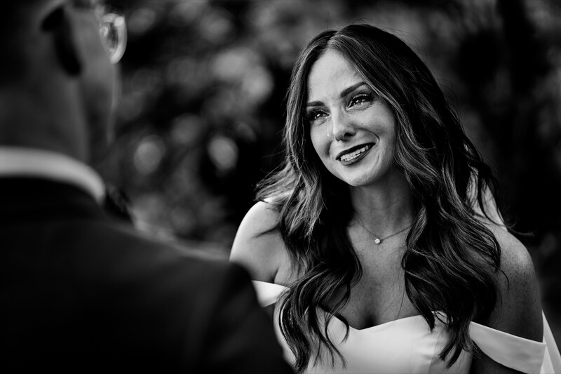 Woman with long dark wavy hair smiling at a man in black and white portrait photography.