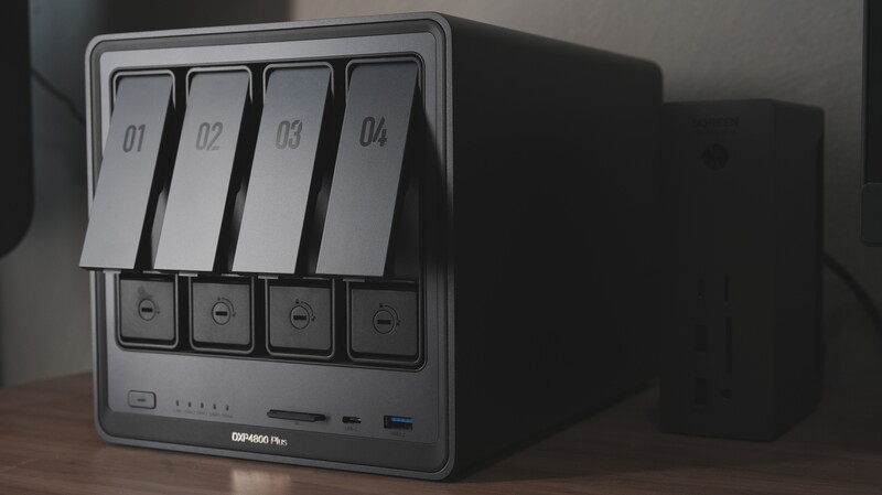 Four-bay NAS enclosure with labeled drive bays and front-mounted controls on wooden surface.