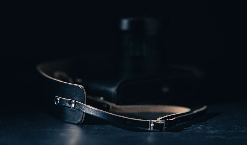 Leather camera strap draped on dark surface with camera body blurred in background.
