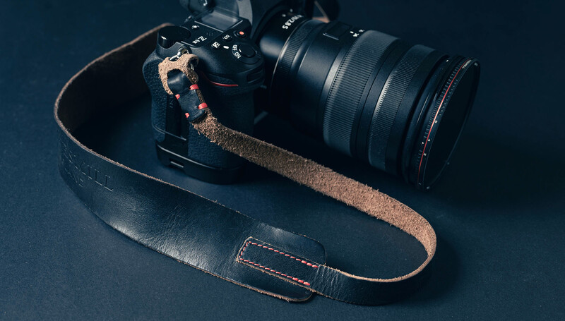 Professional camera with attached lens and weathered leather strap on dark blue background.