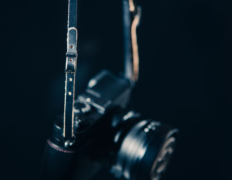 Vintage film camera strap and lens in sharp focus against dark background.