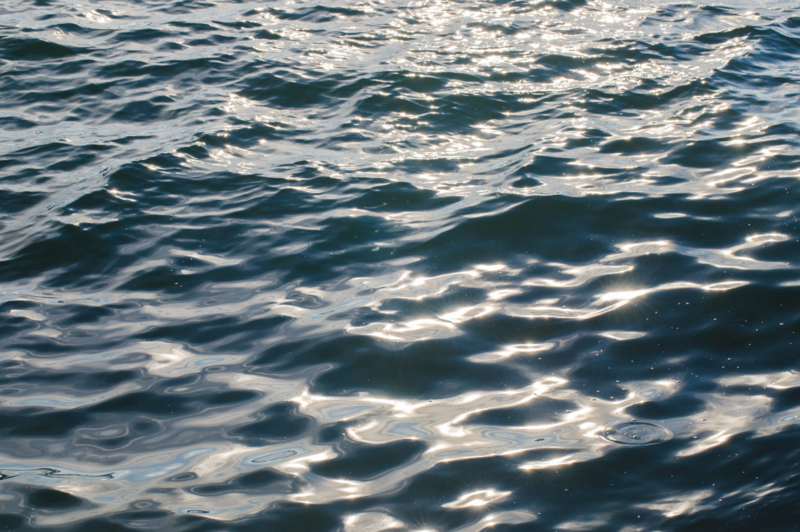 Sunlit ocean water with small waves and ripples creating a textured surface pattern.