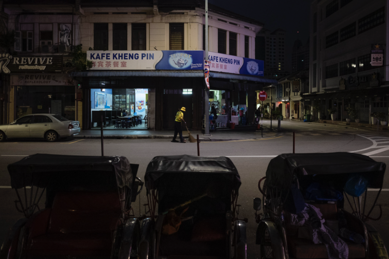 Nighttime street scene with illuminated storefront and parked vehicles in foreground.