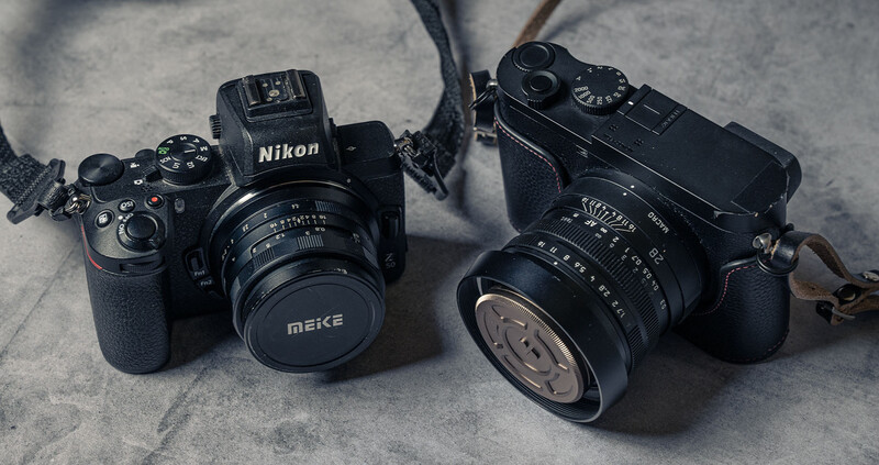 Two vintage film cameras with manual lenses arranged on a textured gray surface, one with a Nikon body and Meike lens, the other with a rangefinder-style body and Kiev lens.
