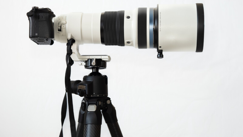 White telephoto lens mounted on black tripod with camera body attached.