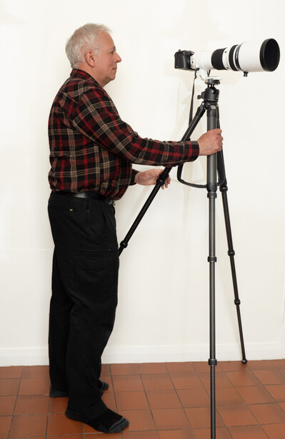 Photographer holding a telephoto lens mounted on a tripod with head.