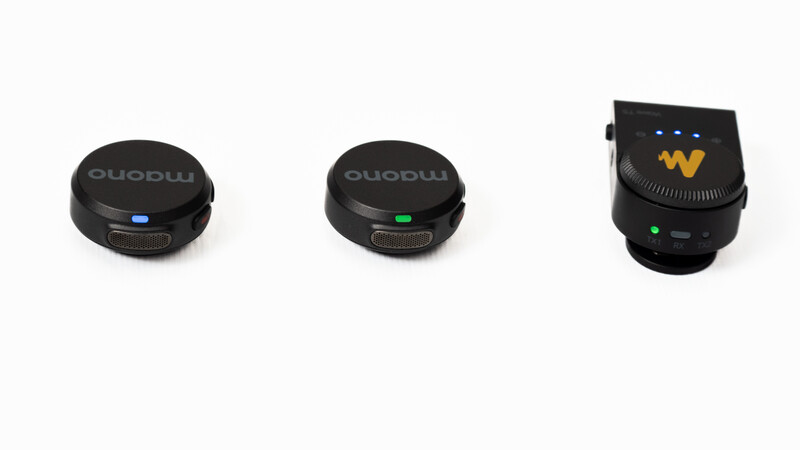 Three black wireless microphone transmitters displayed against a white background, each with different colored indicator lights.