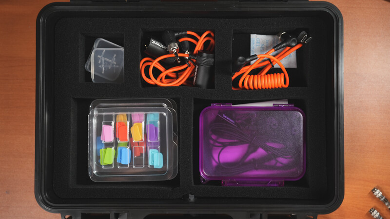 Organized gear case with orange cables, sticky notes, and purple protective pouches on black foam insert.