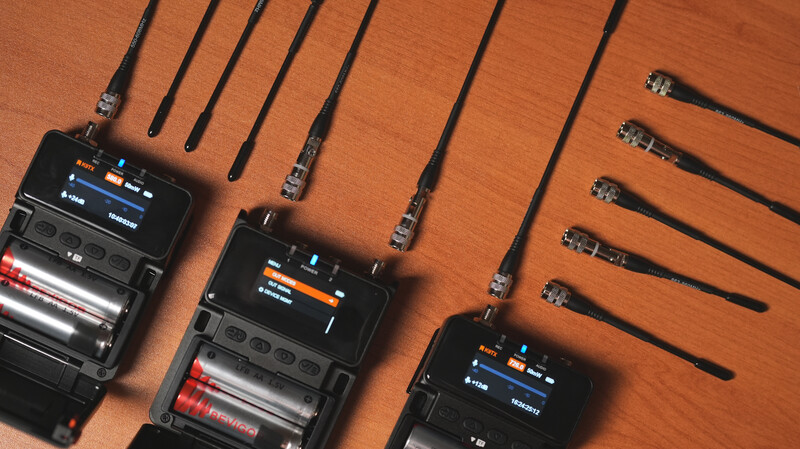 Three wireless microphone receivers and transmitters arranged on an orange wooden surface with coiled cables.