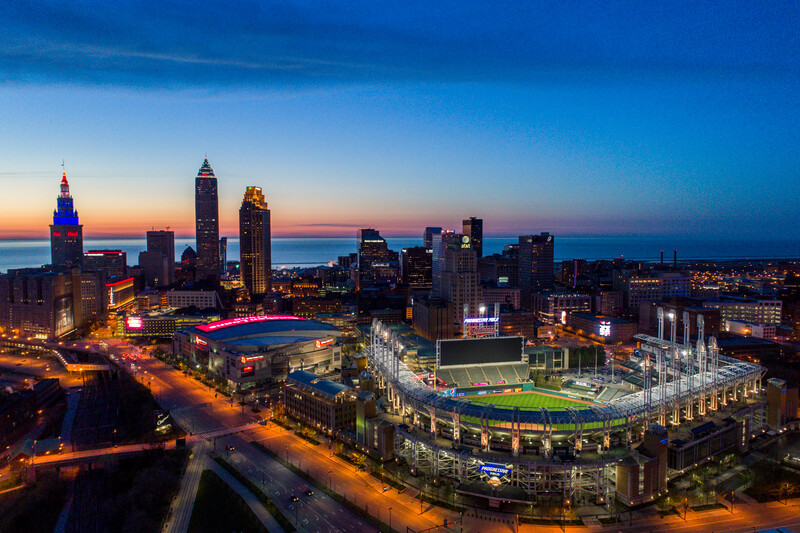Downtown city skyline at dusk with illuminated skyscrapers and two sports stadiums in the foreground.