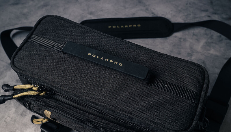 PolarPro camera bag and shoulder strap in black with gold accents on concrete surface.