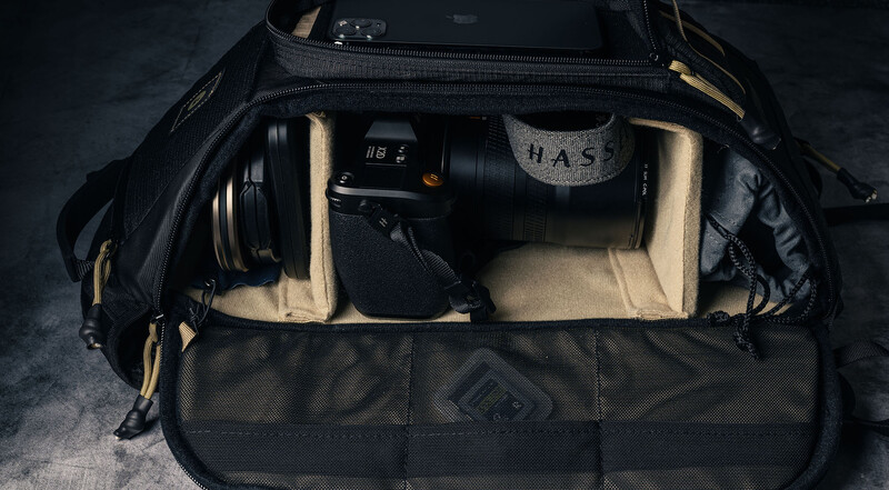 Camera bag interior organized with cream-colored dividers holding telephoto lens, camera body, and accessories.