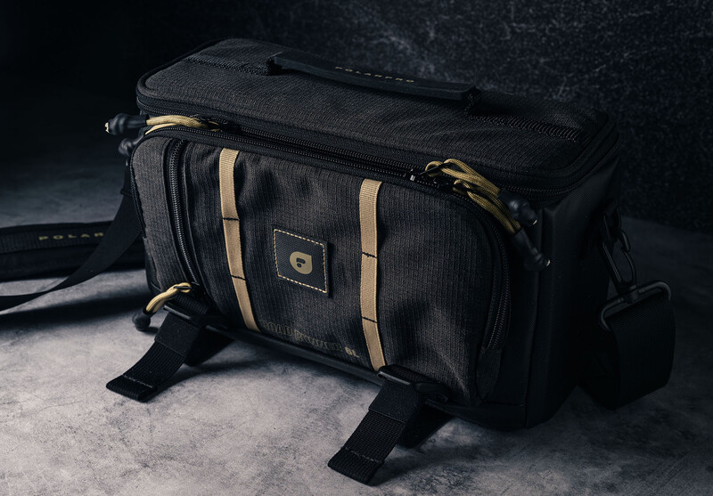 Black camera bag with tan straps and weathered concrete surface background.