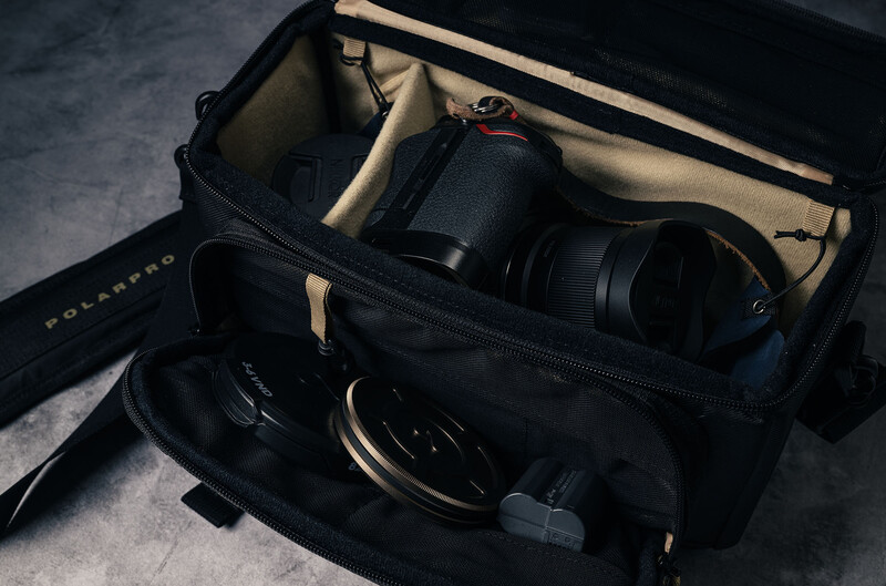 Open camera bag displaying organized photography gear including camera body, lenses, and accessories on neutral fabric lining.