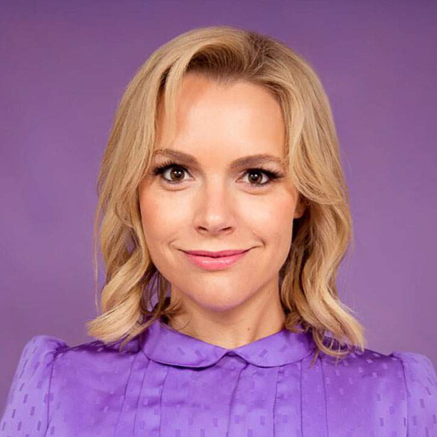 Professional headshot of a woman with blonde wavy hair against a purple background.