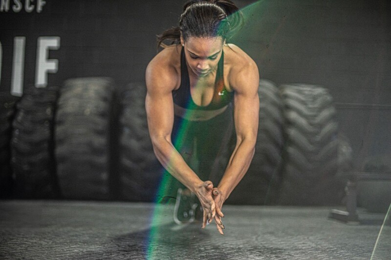 Athletic woman in green tank top preparing hands before exercise at gym with large tires in background.