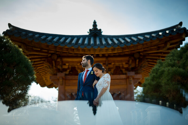 Bride and groom posing in front of a traditional Asian pagoda with upturned eaves.