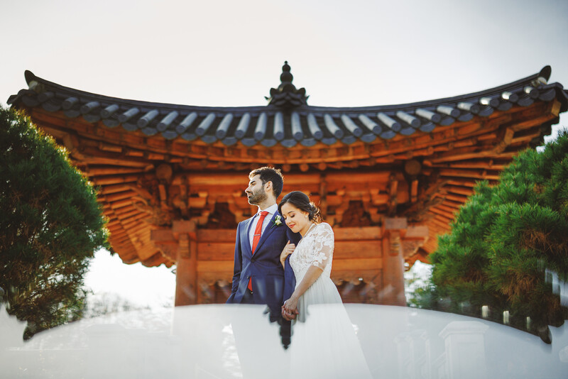 Bride and groom pose together in front of an ornate orange wooden temple with curved eaves.