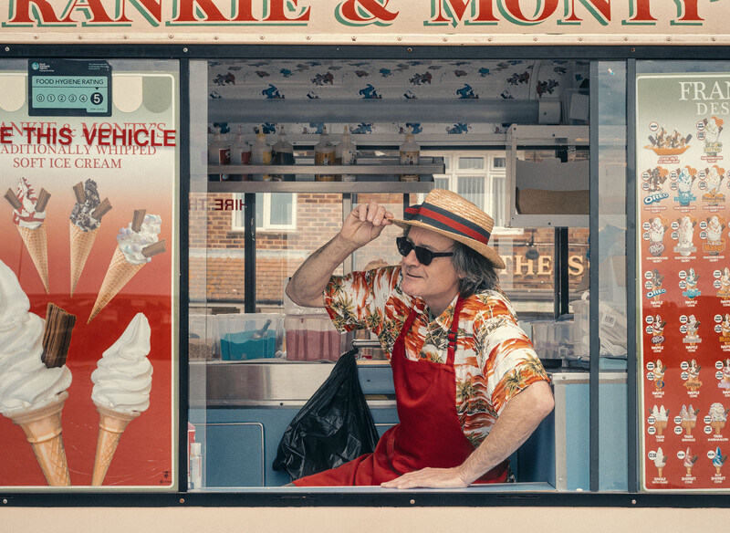 Mannequin dressed in red apron and patterned shirt adjusting straw hat in storefront window display.