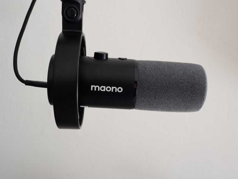 Maono condenser microphone with shock mount and foam windscreen against neutral background.