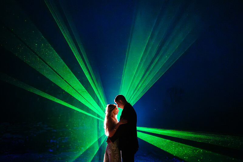 Couple kissing silhouetted against green and blue laser light rays emanating from behind them.