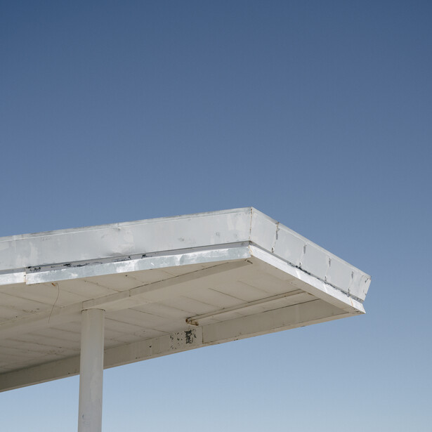 Minimalist architectural photograph of a concrete canopy structure against a clear blue sky.