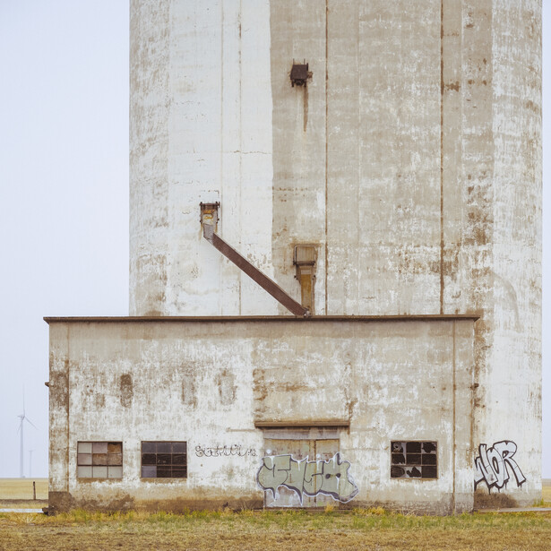 Weathered concrete grain elevator with rust-stained metal chute and graffiti tags on lower section.