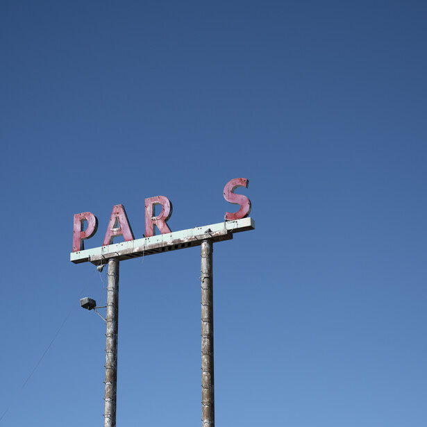 Vintage neon sign reading 'DAR'S' mounted on tall poles against a clear blue sky.