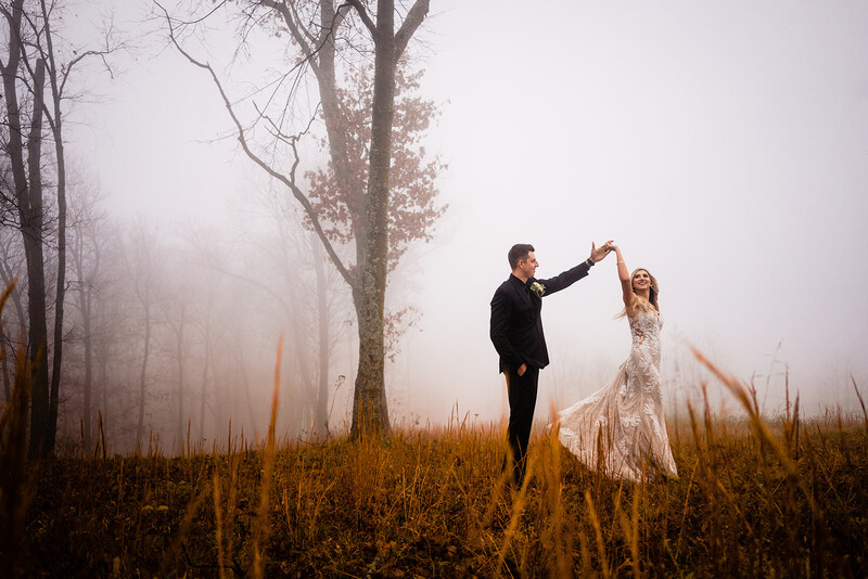 Groom and bride dancing in a misty field with bare trees and golden dried grass.