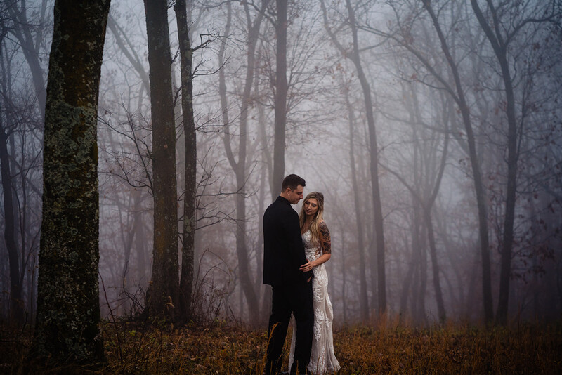 Couple embracing in a misty forest surrounded by bare trees and autumn leaves.