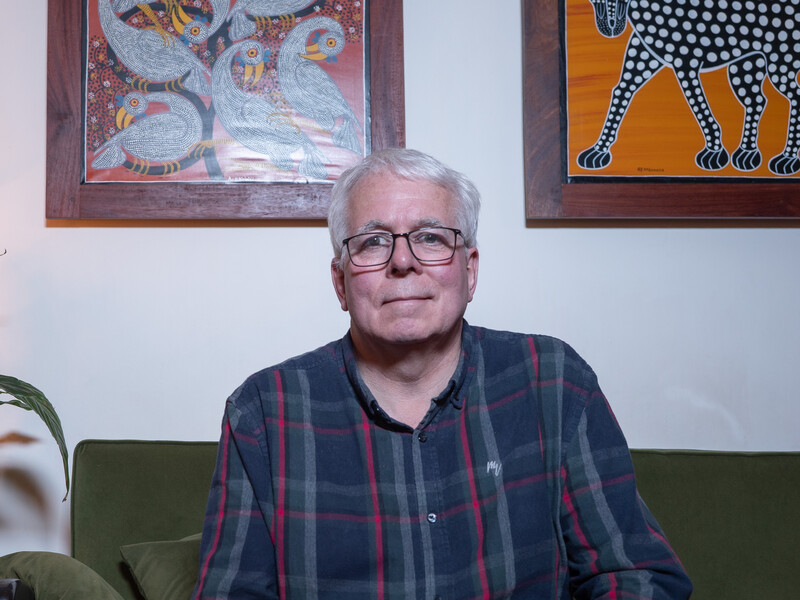 Middle-aged man with gray hair and glasses wearing a plaid shirt seated on a green couch.