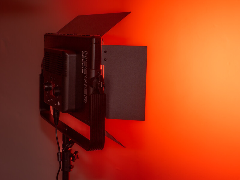 Professional LED panel light with barn doors and diffusion panel against warm orange background.